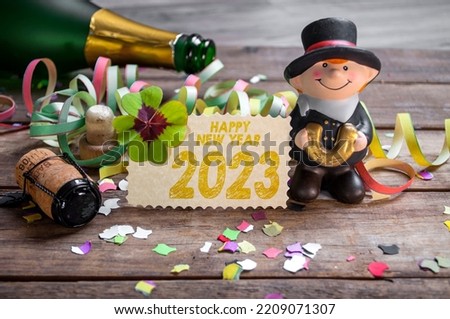 Wooden hang tag and slate with four leaf clover and sparklers with the german words for happy new year - frohes neues jahr 2023 on wooden weathered background