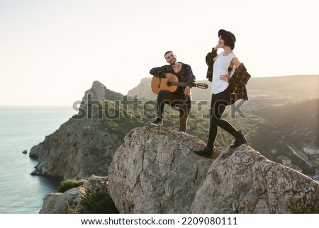 Couple in love on a mountaintop overlooking the sea. A man plays the guitar, a woman dances and sings
