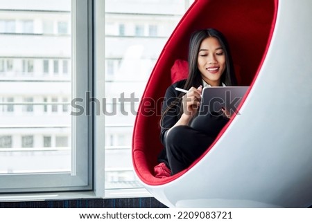 Young woman drawing on digital tablet at office sitting in chill zone in comfortable chair Royalty-Free Stock Photo #2209083721