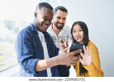 Happy coworkers looking at phone in office. Students share smartphone at university Royalty-Free Stock Photo #2209083731