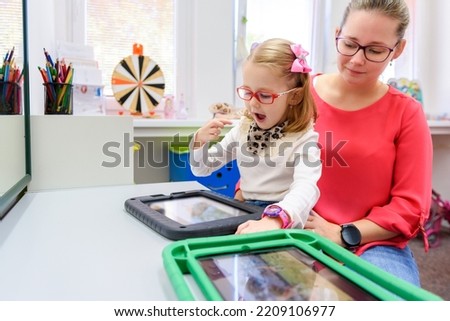 Non-verbal girl living with cerebral palsy, learning to use digital tablet device to communicate. People who have difficulty developing language or using speech use speech-generating devices. Royalty-Free Stock Photo #2209106977