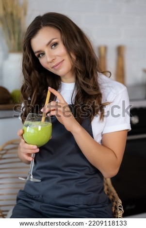 young housewife on a diet drinks fresh detox smoothie from green vegetables and fruits from a glass