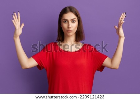 It is too much. Doubting young pretty brunette girl in red t-shirt shows width of something. Woman thinks it is a big price for item. Ask for extra discount. Posing over purple background Royalty-Free Stock Photo #2209121423
