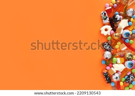 Halloween orange background with copy space on left, assorted candies on right: traditional eyeballs chocolates, jelly worms, gummy ghosts. Happy Halloween holiday sale and trick-or-treat concept.