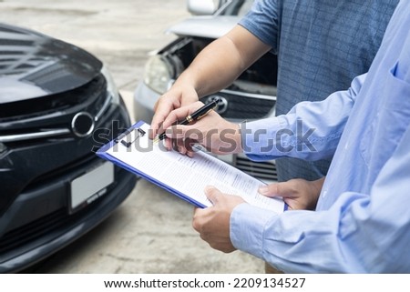 insurance officer writing on clipboard while insurance agent examining black car after accident
