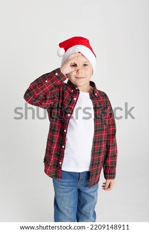 The charming seven year old boy in red Santa Claus cap smiles, having stretched hands up. The photo is executed by isolated