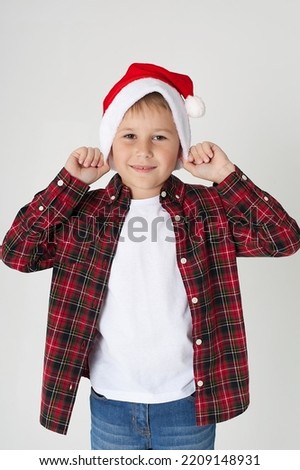 The charming seven year old boy in red Santa Claus cap smiles, having stretched hands up. The photo is executed by isolated