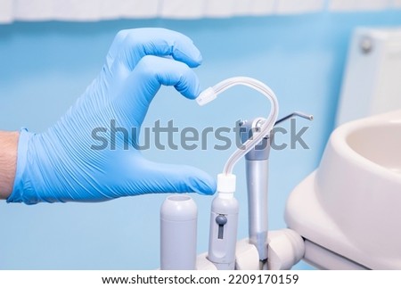 Dental equipment. A hand in a blue glove and a saliva ejector in the form of a heart. Love for dentistry.