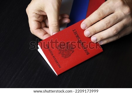 Russian military ID in male hands on wooden table. Translation of inscription Military ID card, Russian Federation. Concept of mobilization in Russia