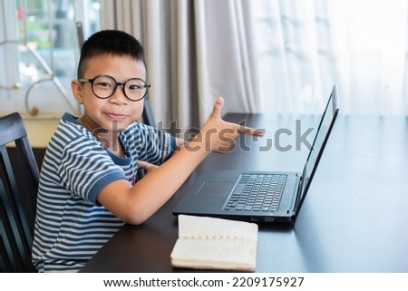 Eight-year-old Asian boy wearing glasses sits at work using a laptop.