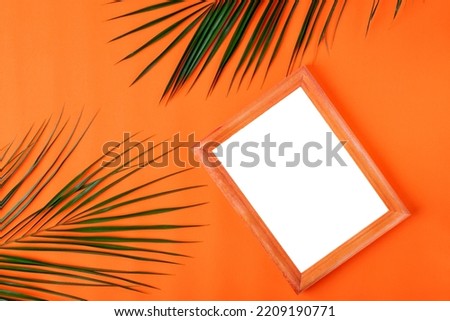 Picture frame mockup and palm leaves on orange background. Flat lay template. Minimalist summer backdrop with copy space