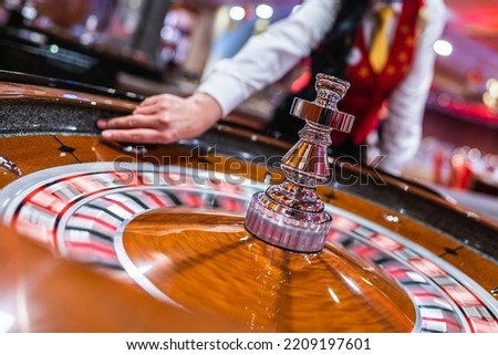 The dealer holds a ball and spins the roulette wheel in a casino. Royalty-Free Stock Photo #2209197601