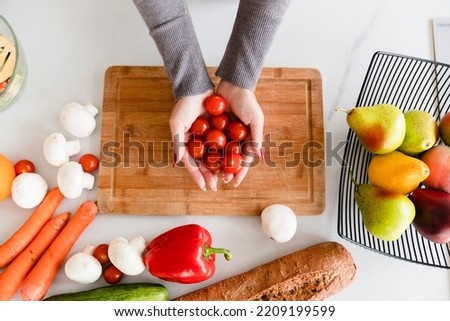 Cropped top view photo of cooking kitchen table, while chef female housewife holding tomatoes, preparing doing making vegetable salad, vegan vegetarian food