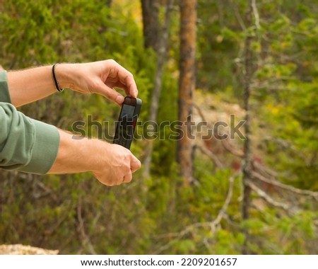 man takes pictures on his phone in the mountains, a hand holding a phone for a photo shoot, cellular communication in nature, a memorable photo on vacation, a hike in the forest. 