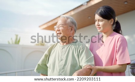 Senior elder Asian man having a physical therapy by walking with cane staff support. Professional caregiver taking an elder Asian old man walking at the park.