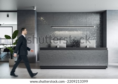 Side view on businessman walking by stylish dark furniture reception area in grey shades office Royalty-Free Stock Photo #2209213399