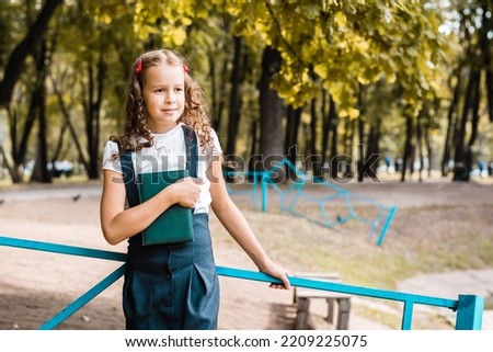A pupil in a school uniform with a book walks on a warm day in the park
