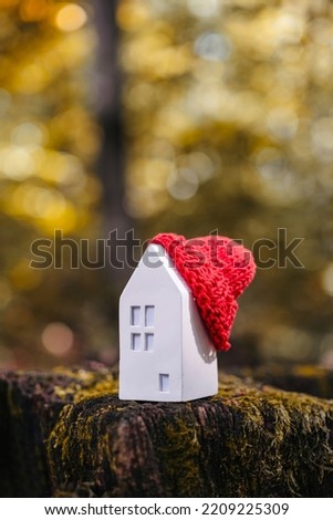 Miniature house in a red hat on an autumn background with moss and yellow leaves. The concept of passive house heating. Thermal insulation of a building or dwelling. Energy crisis. Royalty-Free Stock Photo #2209225309