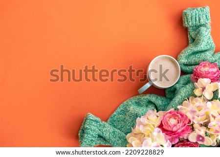Cup of coffee, flowers and knitted element on orange background, flat lay.