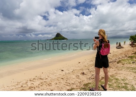 Woman taking photos of Mokoliʻi from the shores of Kualoa Regional Park

