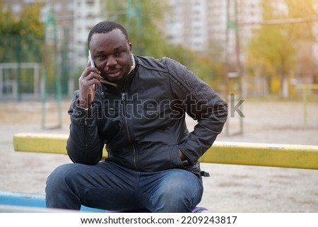 African american man sits at sport ground and speaks on smartphone