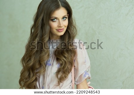 Portrait of a beautiful girl with flowing curly hair, smiling, looking at the camera on a light background. Healthy Hair concept. High quality photo