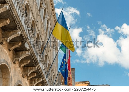 The flag of Ukraine, the flag of the European Union, the flag of Italy and Venice are fluttering in the wind on the wall of an old historical building against the blue sky in the city of Venice