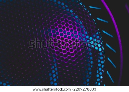 Colorful light of computer fan shines through the holes of protective grid. illumination glows in the dark. abstract futuristic background. led lighting of gaming pc