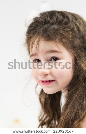 Beautiful little girl with long, curly hair and beige dress posing with light grey background 