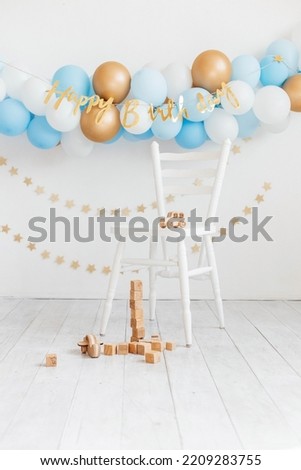 Beautiful photo zone for a birthday with blue and white balloons and the inscription Happy Birthday on a white wall. White chair with wooden eco toys. Wooden cubes and a wooden children's car