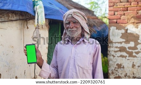 Old Asian man smiling and showing a green screen cell phone with rural village life concept background.