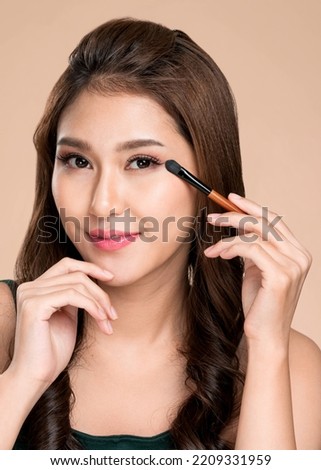 Portrait of ardent young woman with healthy fair skin applying her eyeshadow with brush. Female model with fashion makeup. Beauty and makeup concept.