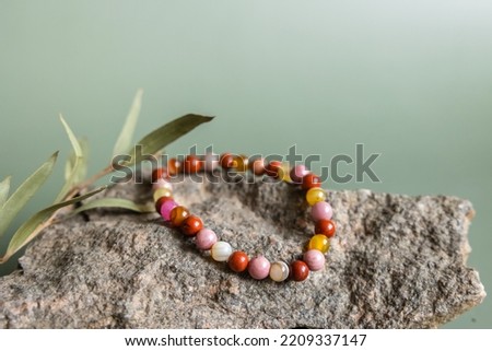 Bracelet made of natural pink agate stones beads on green background. Handmade jewelry. Woman exoteric accessories. Talismans and amulets. Selective focus