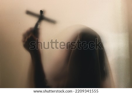 Horror ghost woman holding a cross behind the matte glass. Halloween festival concept.
