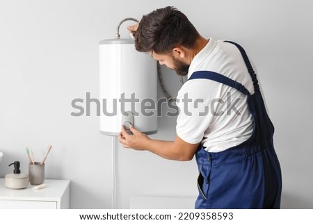 Male plumber adjusting boiler in bathroom Royalty-Free Stock Photo #2209358593