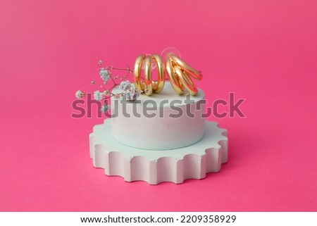 Showcase pedestal with trendy earrings and gypsophila flowers on pink background