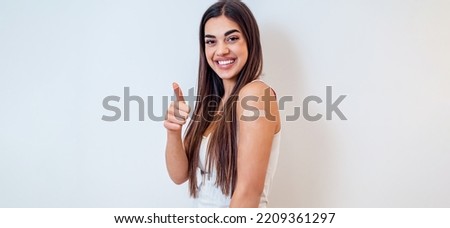 Picture of smiling, brunette, young adult woman, giving thumbs up, after a successful vaccination.