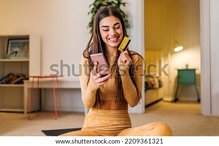 Cheerful brunette woman, using her credit card to buy something online, on her phone. Royalty-Free Stock Photo #2209361321