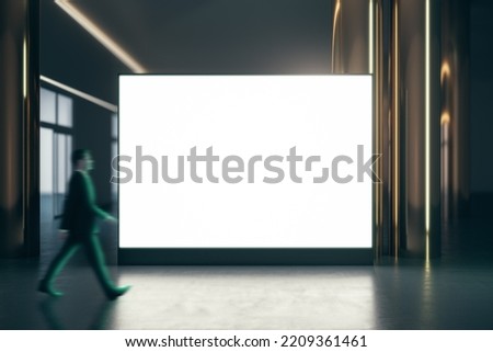 Walking businessman by blank white illuminated big screen with place for your logo or text between golden pillars with glossy floor on dark empty room background, mock up Royalty-Free Stock Photo #2209361461