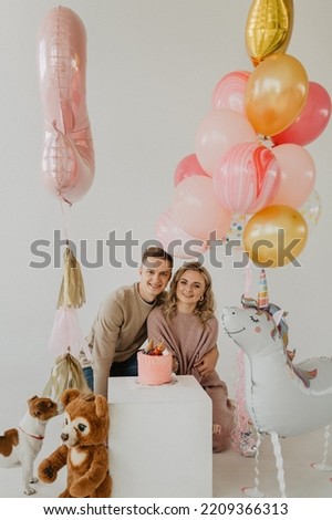 A little girl with mom and dad hug and kiss on the background of a cake and balloons. Cake smash