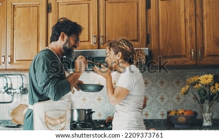 One happy real couple at home enjoying life together and relationship. Man giving food to woman to taste. Male people cooking for his wife. Male and female enjoying leisure activity indoor in kitchen Royalty-Free Stock Photo #2209373761