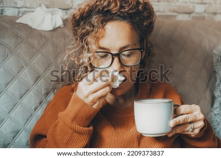 Sick woman at home blowing nose and take care of influenza virus disease. One female people using paper tissue and drink herbal tea medicine alone at home. Concept of flu cold in winter season indoor Royalty-Free Stock Photo #2209373837