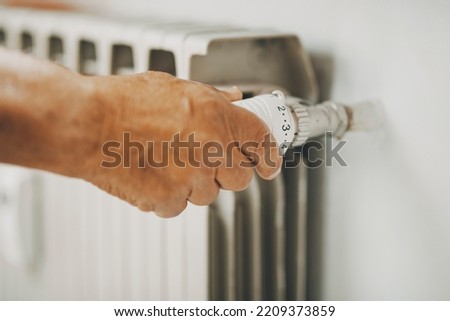 Close up of old man hand closing  heating home thermostat for gas energy saving. Concept of bills and heat crisis costs. People adjusting radiator supply to save money during winter Royalty-Free Stock Photo #2209373859