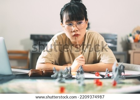 Role playing tabletop and board game hobby concept. Young adult asian woman enjoying with storytelling. Blur foreground with monster miniatures and dice component. Royalty-Free Stock Photo #2209374987