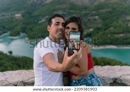 Young couple consisting of a boy and a girl taking a selfie with their mobile phone held vertically showing behind the idyllic landscape of the turquoise water swamp. The mobile phone is in focus