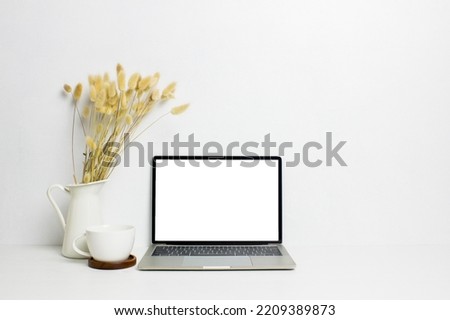 A mock up computer with brown natural flowers and coffee cup on white table. 