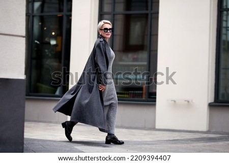 Elegant Mature woman walks city street , wears stylish clothes, gray wool coat, long dress, black shoes and glasses. Trending outfit Royalty-Free Stock Photo #2209394407