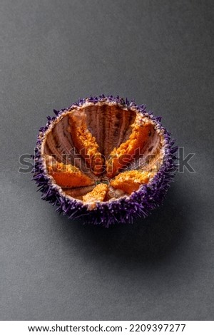 Half of the shell of a sea urchin lies on a dark, paper background. You can see the fresh edible part.
