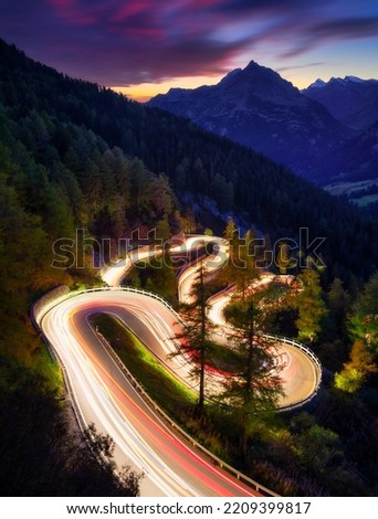 The mountain pass of Maloja, Switzerland. A road with many curves among the forest. A blur of car lights. Landscape in evening time. Large resolution photo for travel Royalty-Free Stock Photo #2209399817