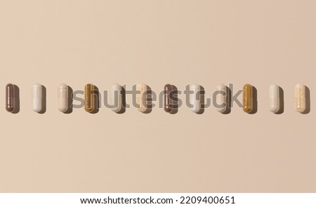 Mix of medical capsules in a line on light beige top view, hard shadows. Preventive medicine and healthcare, dietary supplements and vitamins.  Assorted pharmaceutical medicine capsules Royalty-Free Stock Photo #2209400651